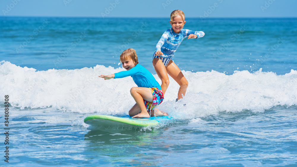 快乐的男孩和女孩-年轻的冲浪者在一个冲浪板上玩得很开心。孩子，积极的家庭生活方式