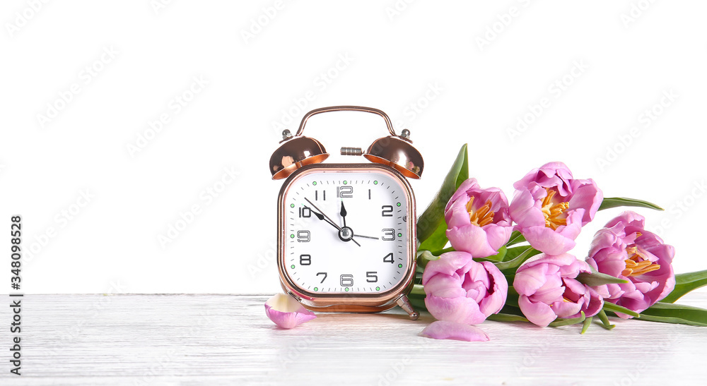 白色背景下的闹钟和桌子上的鲜花。春天的时间