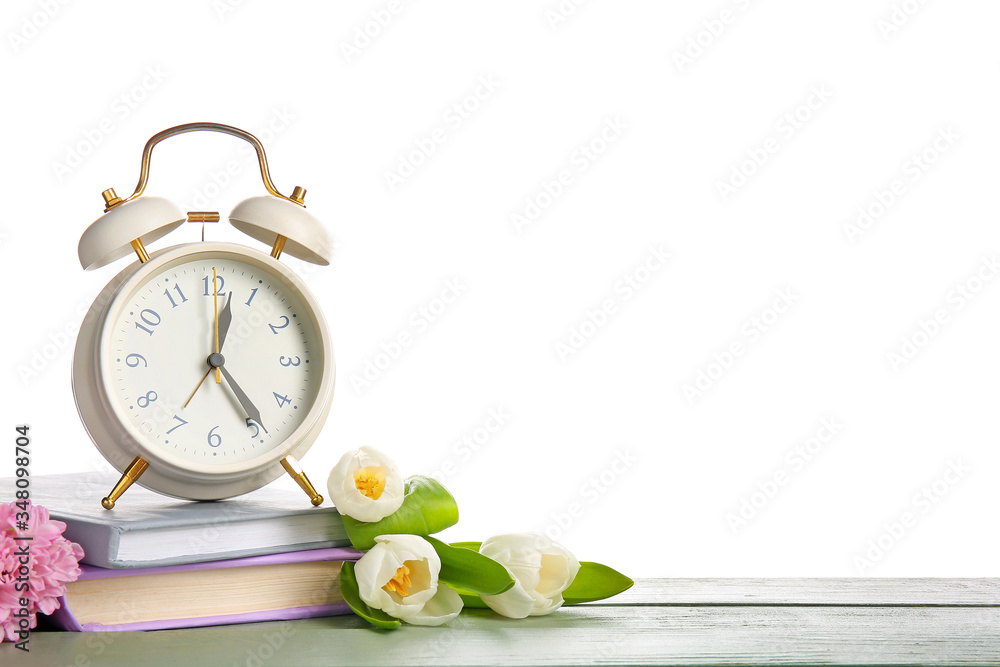 白色背景下的闹钟、桌子上的书和花。春天的时间