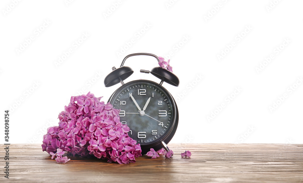 白色背景下的闹钟和桌子上的鲜花。春天的时间