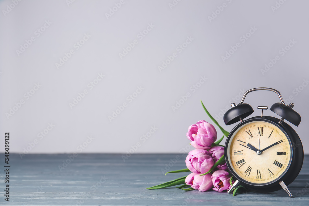 闹钟和桌子上的鲜花。春天的时间