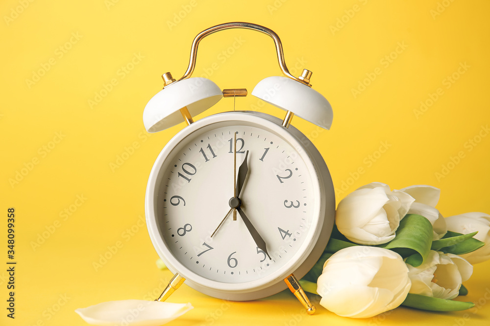 Alarm clock and flowers on color background. Spring time