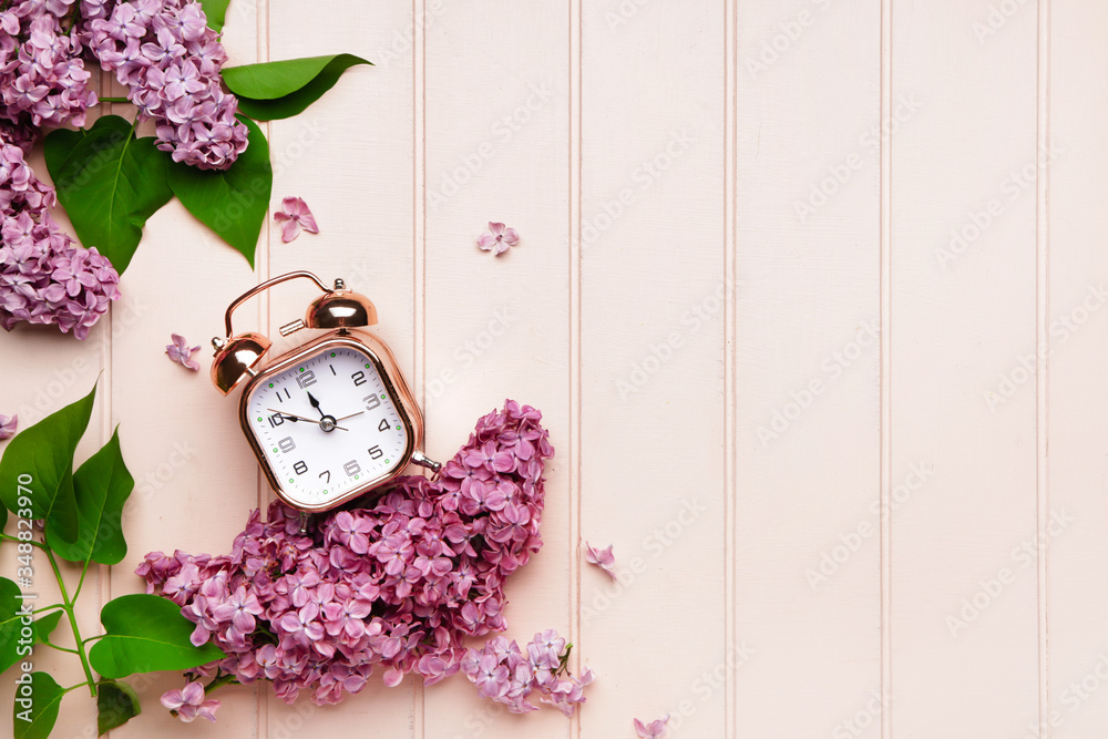 Alarm clock and flowers on wooden background. Spring time