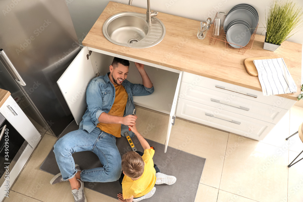 Little son helping his father to repair sink in kitchen