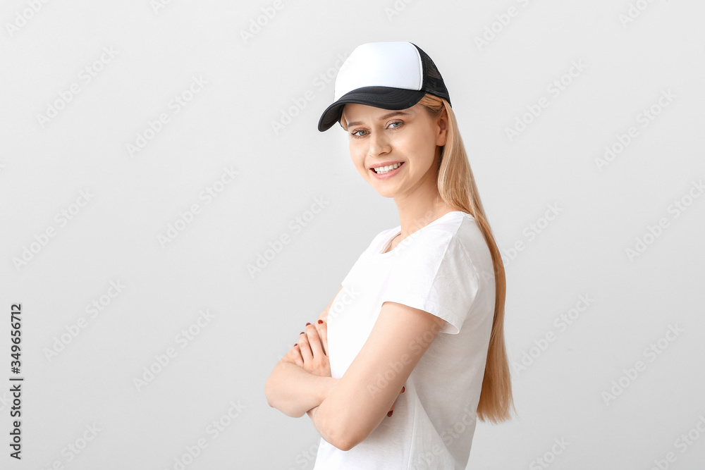 Beautiful young woman in stylish cap on light background