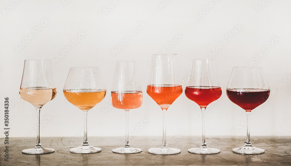 不同色调的玫瑰酒，装在带梗的玻璃杯中，在混凝土上从浅色到深色排列