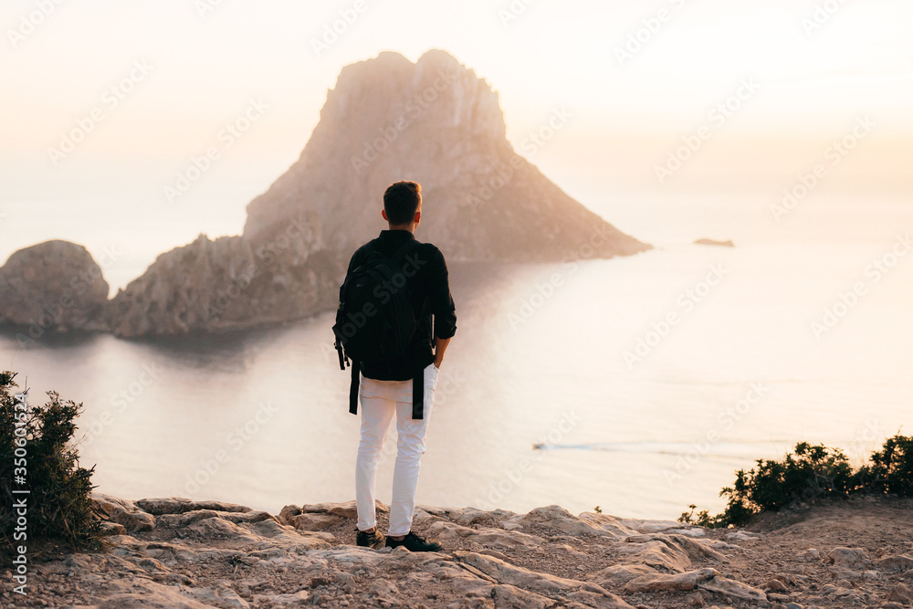 西班牙，伊维萨岛，男人背着背包旅行，日落时眺望大海和埃斯韦德拉岛。