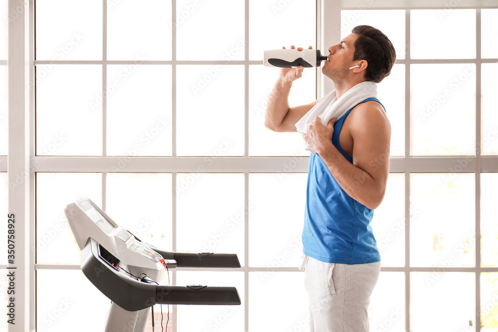 Young man drinking water after training in gym