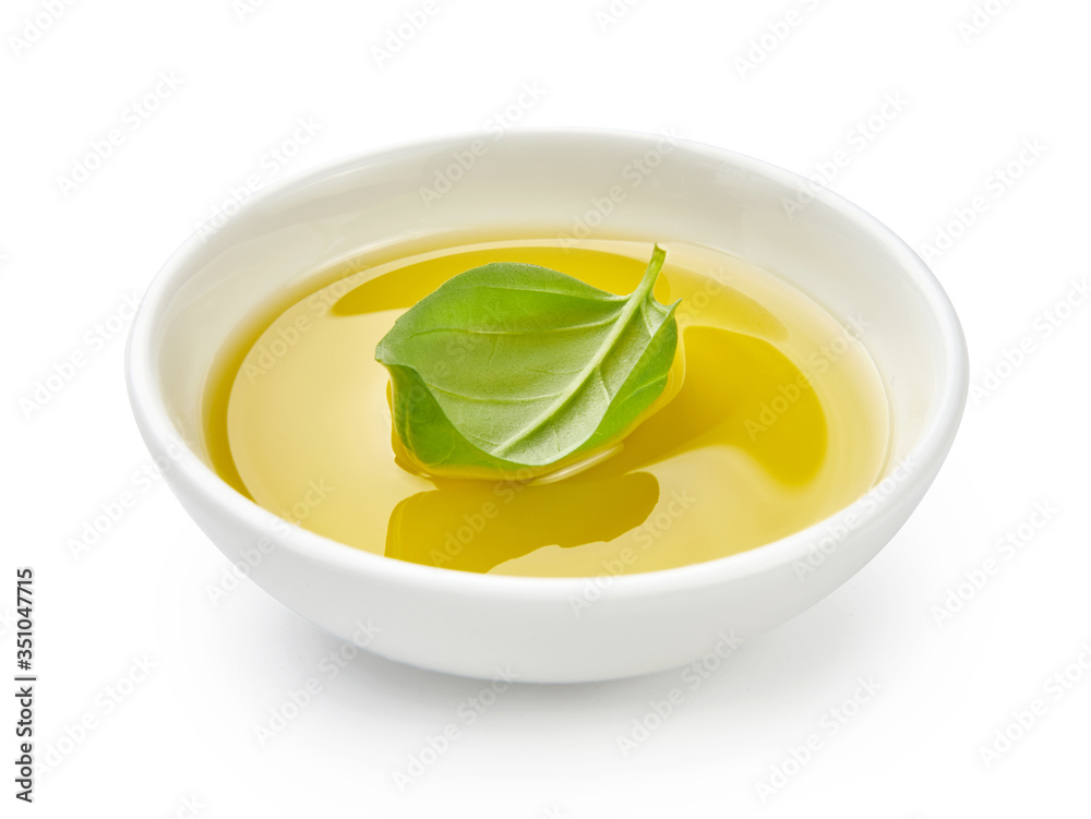 白色碗中的橄榄油或植物油。油中有隔离在白色背景上的罗勒叶。