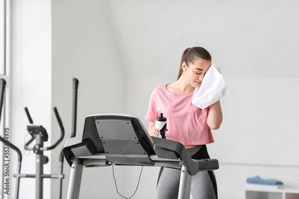 运动型年轻女子在健身房跑步机上训练后休息
