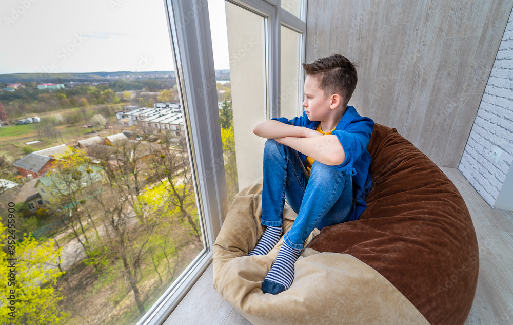 男孩坐在阳台上的软椅上。大窗户可以看到城市的景色。独自放松。