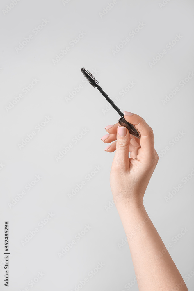 Female hand with mascara on grey background