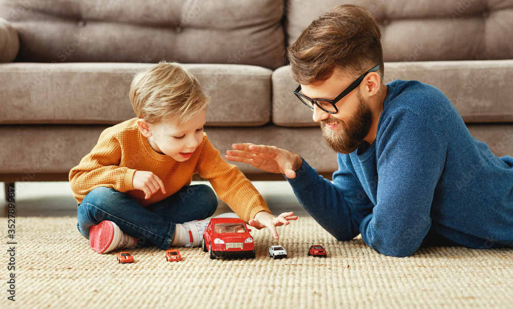 正面的年轻胡子男子和小儿子坐在沙发附近的地板上玩游戏的侧视图