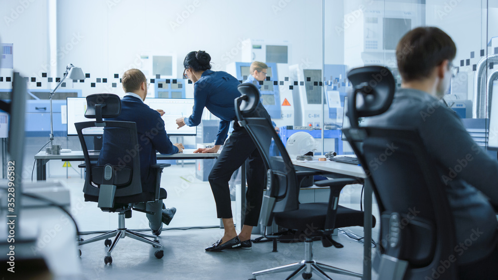 现代工厂：女性项目主管与一位从事计算机工作的男性工业工程师交谈。