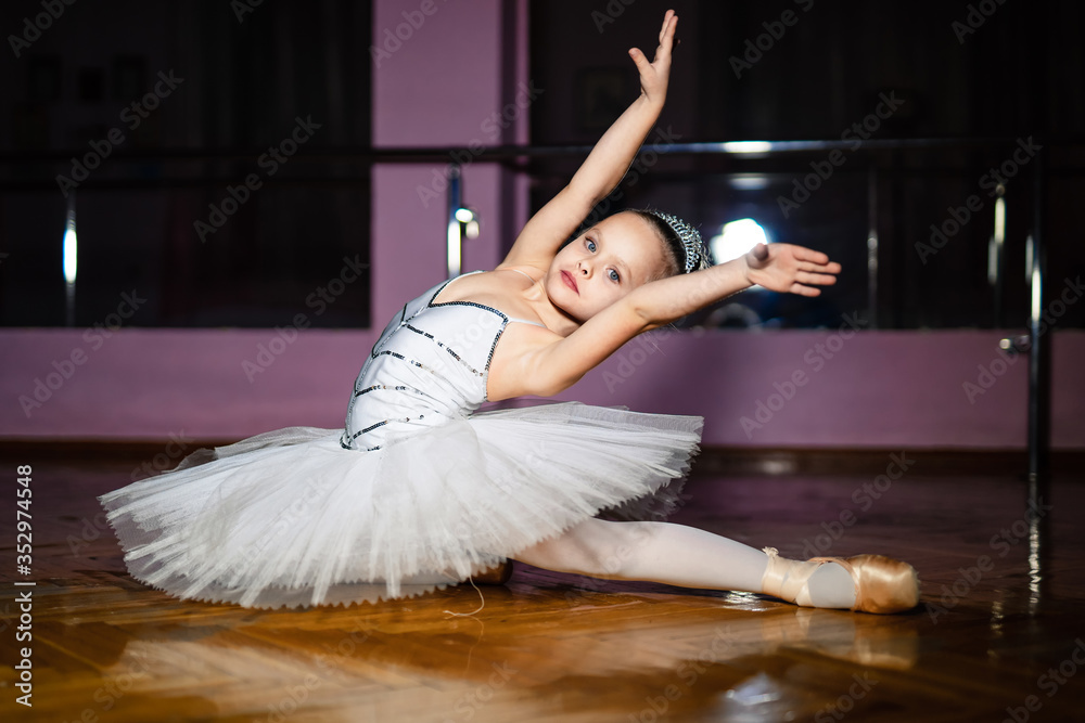 穿着白色紧身连衣裤的可爱小女孩在舞蹈工作室制作新的芭蕾舞动作