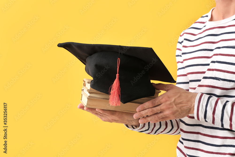 Young man with graduation hat and books on color background
