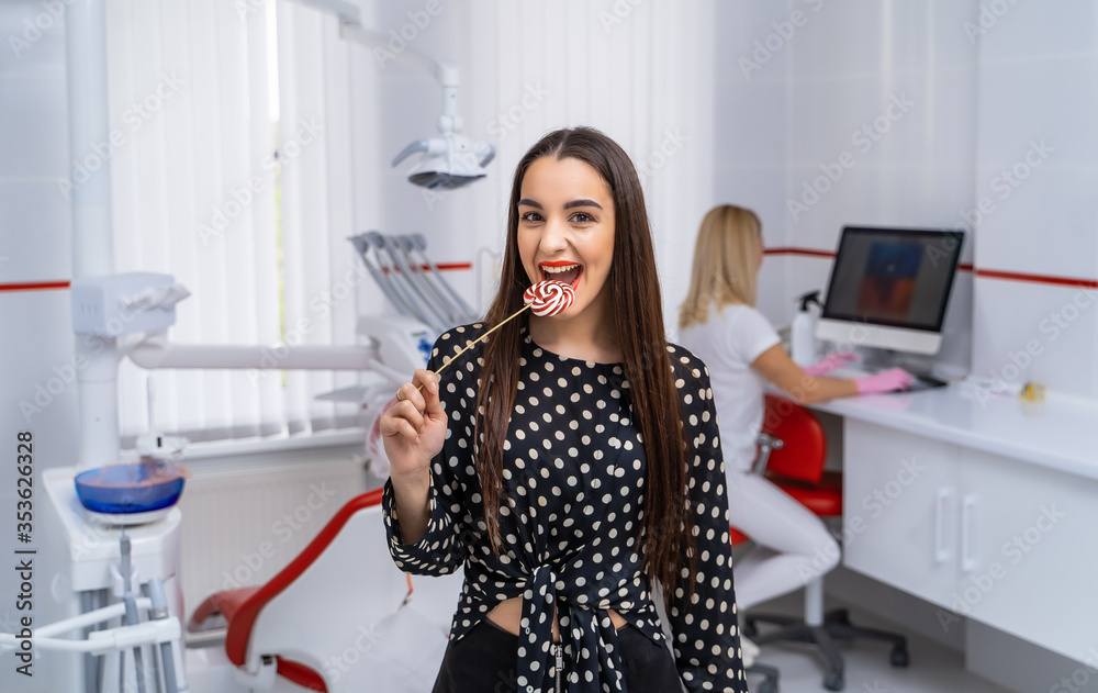 快乐微笑的女孩手里拿着糖果。牙科办公室背景。特写水平