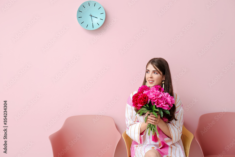 开着美丽牡丹花的年轻女子坐在靠近彩色墙的椅子上