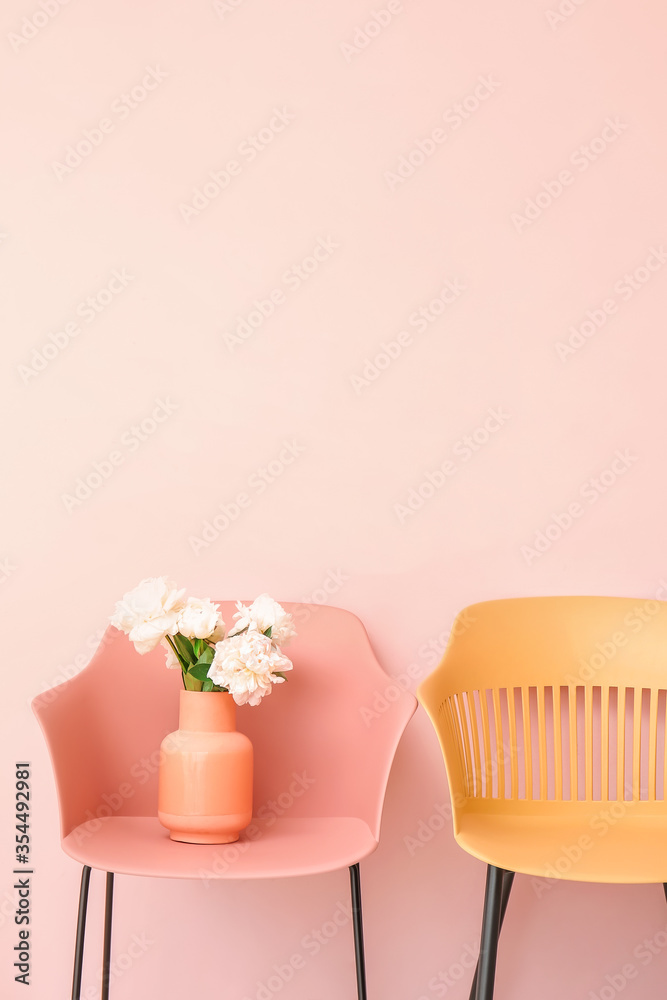靠近彩色墙的椅子上有漂亮的牡丹花的花瓶