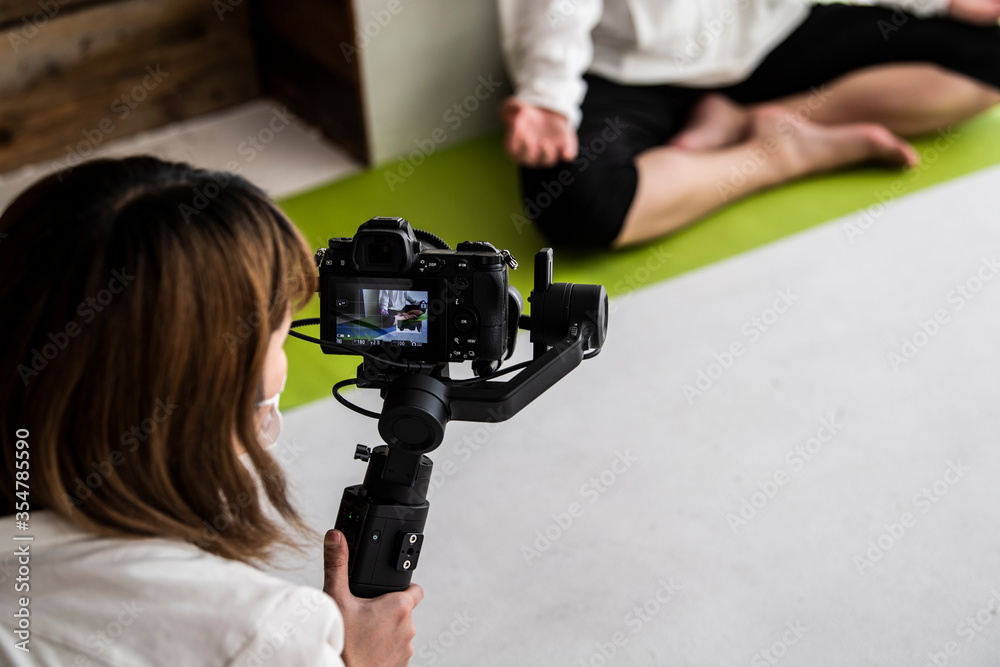動画配信コンテンツ作成のためにカメラマンがヨガをする女性を撮影している。