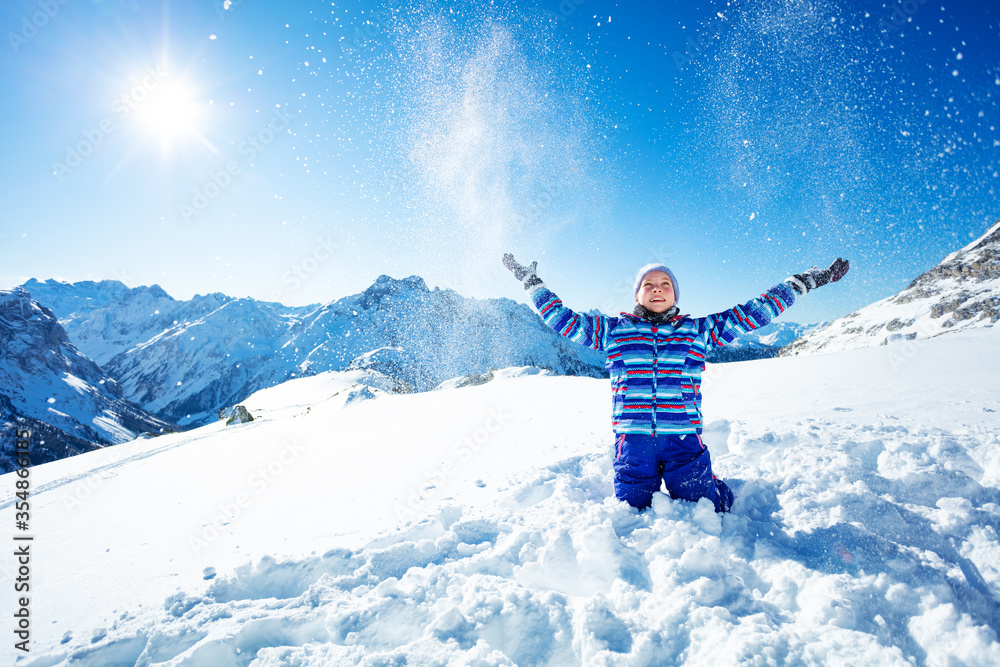 可爱的微笑女孩在阳光明媚的日子里把雪抛向空中，在蓝天和群山上特写