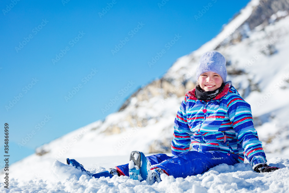 快乐的小女孩穿着冬天的外套，戴着帽子，笑着坐在雪地里
