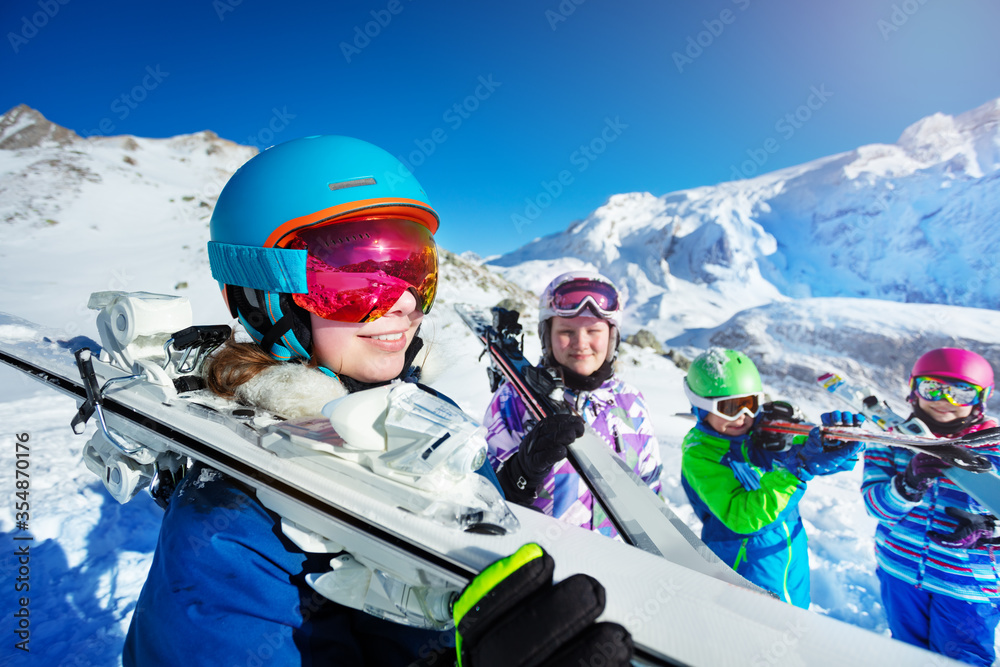 一个十几岁的女孩在山上的肖像，把滑雪板放在肩膀上，站在雪山顶上。