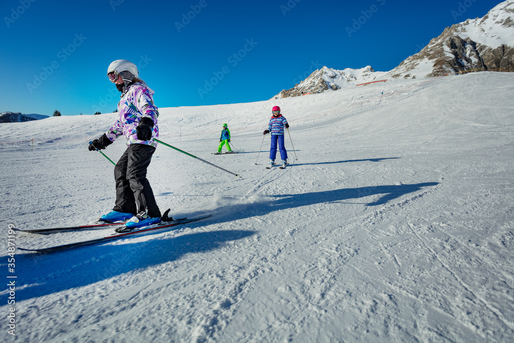 Group of kids in ski school move downhill one after another on wide easy slope
