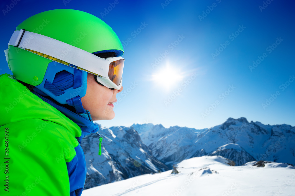 一个戴着滑雪板头盔的男孩在高山山脉的山峰上侧视的近景