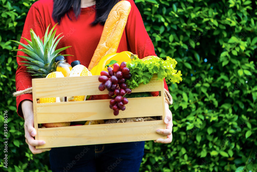 亚洲妇女拿着装有蔬菜的木篮子。篮子里有新鲜蔬菜。在花园野餐