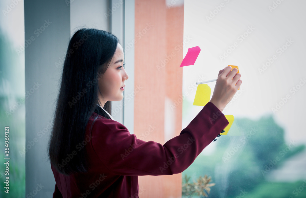 年轻的亚洲女商人在现代办公室的玻璃上写便笺簿的肖像。商业p