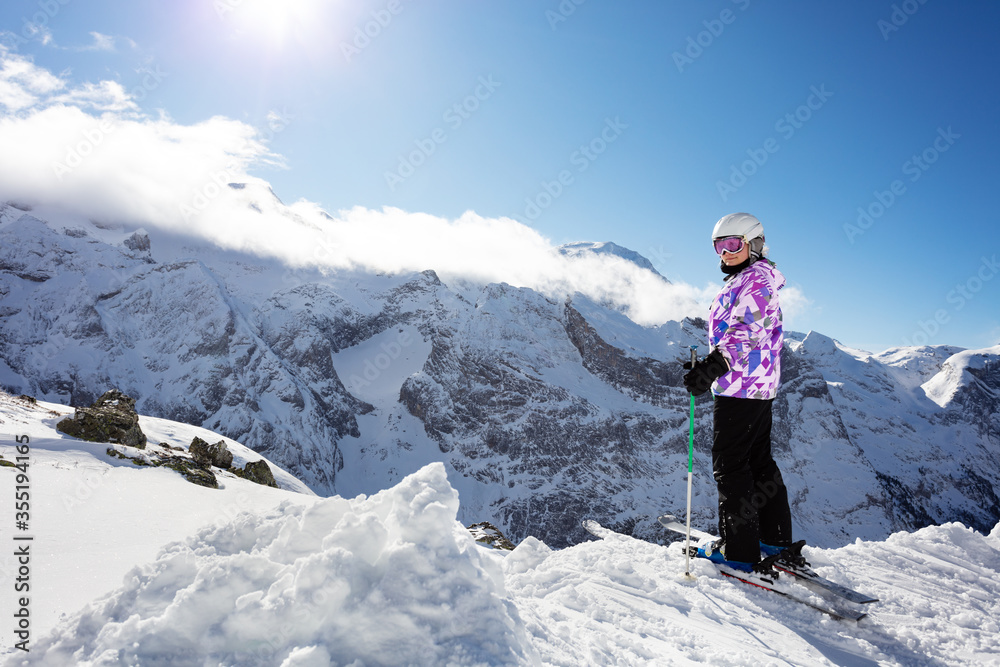 穿着冬季运动服站在高山滑雪场上的快乐少女侧照