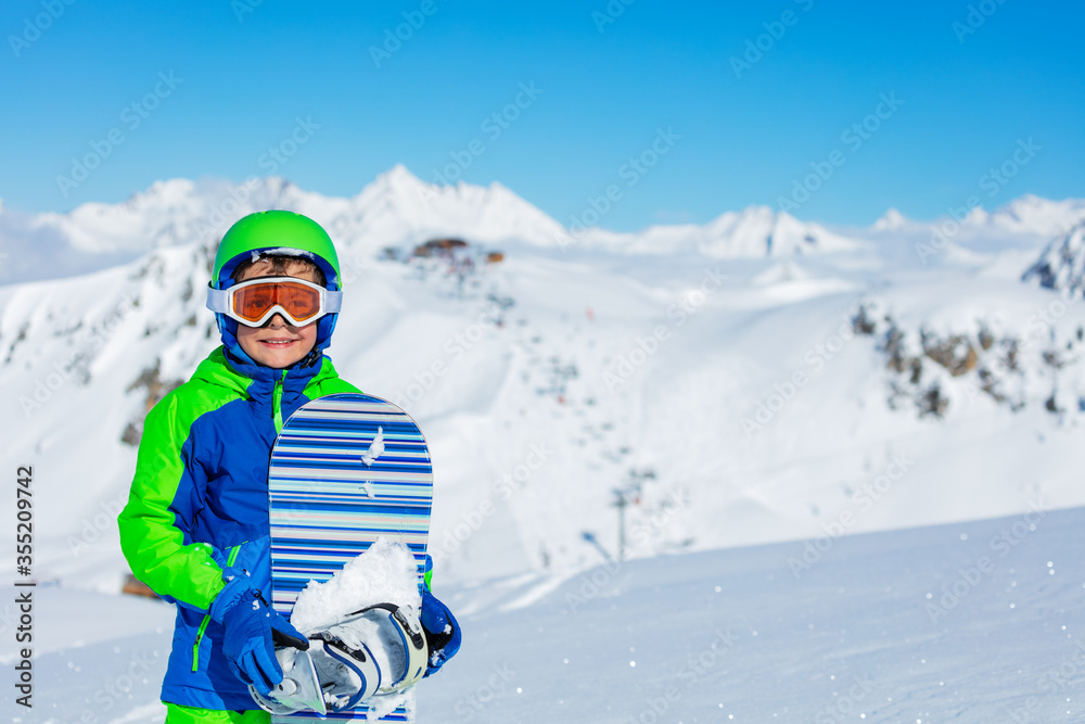 一个戴着运动头盔、戴着滑雪板眼镜的男孩在阳光明媚的山顶上的近景
