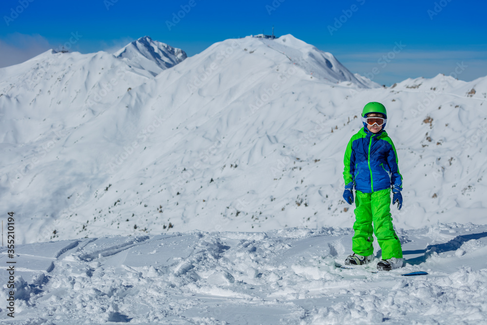 一个男孩戴着亮蓝色和绿色的运动服面具，戴着头盔，站在山上的滑雪板上的肖像