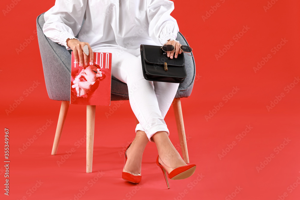 美丽的年轻非裔美国女性，带着时尚的包包和杂志，坐在扶手椅上，穿着彩色ba