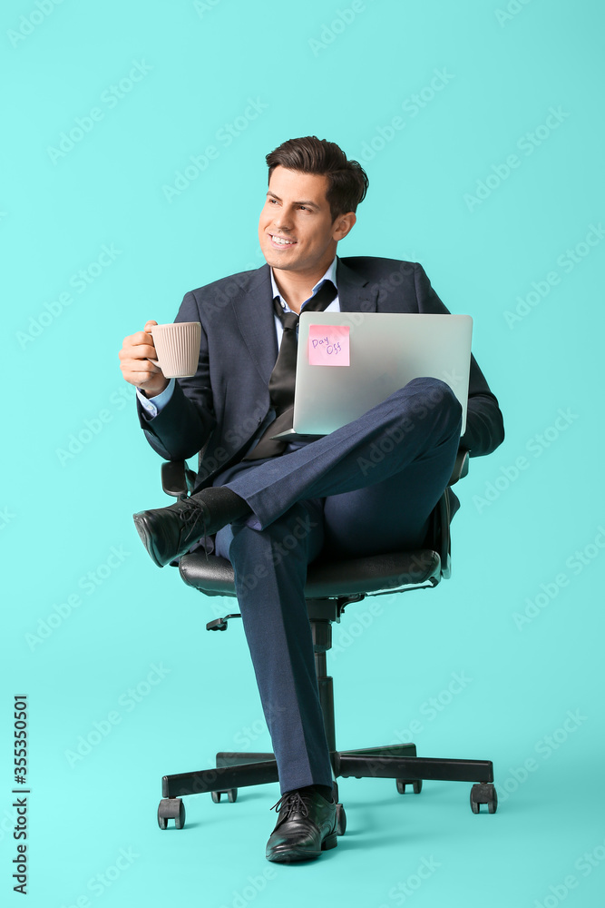 年轻的商人拿着笔记本电脑和咖啡在彩色背景下的椅子上放松