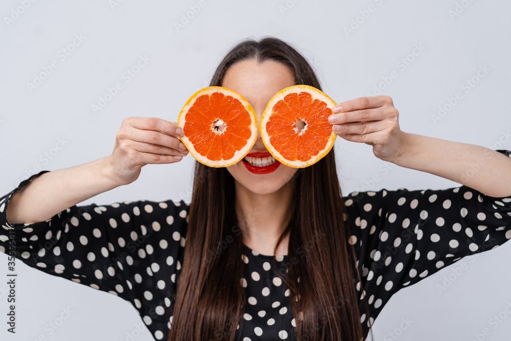 快乐的女孩把葡萄柚的两半举到眼睛附近。疯狂素食主义者的概念。面部表情