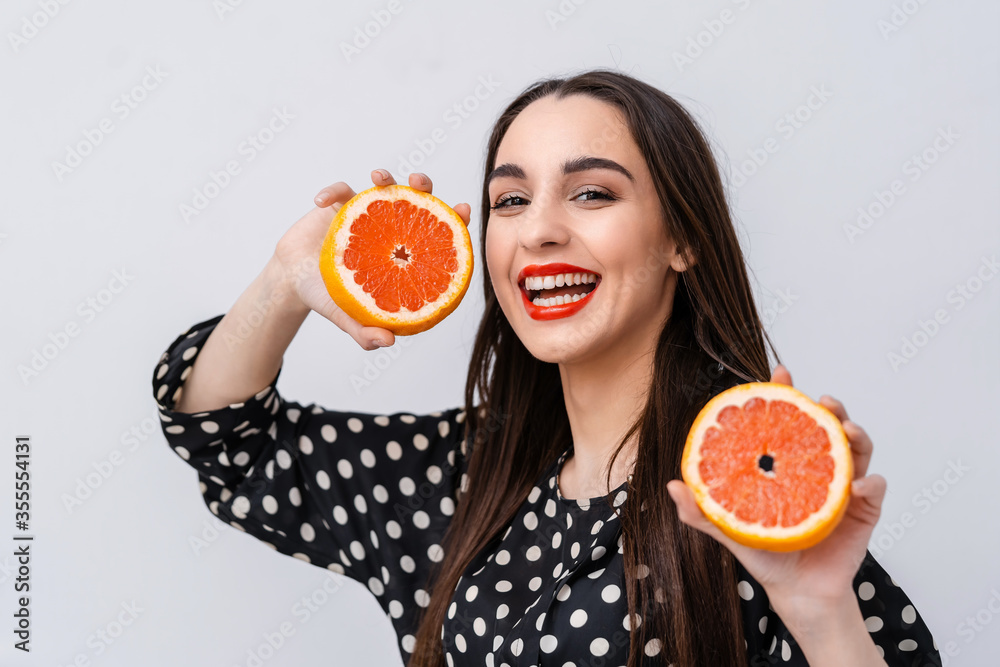 红唇可爱的女人。女人手里拿着两半柑橘类水果，对着镜头。面部表情