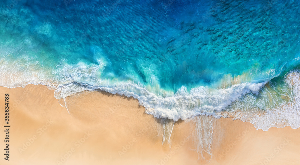 从俯视图中可以看到海滩和海浪作为背景。无人机拍摄到蓝色的水背景。夏天的海景