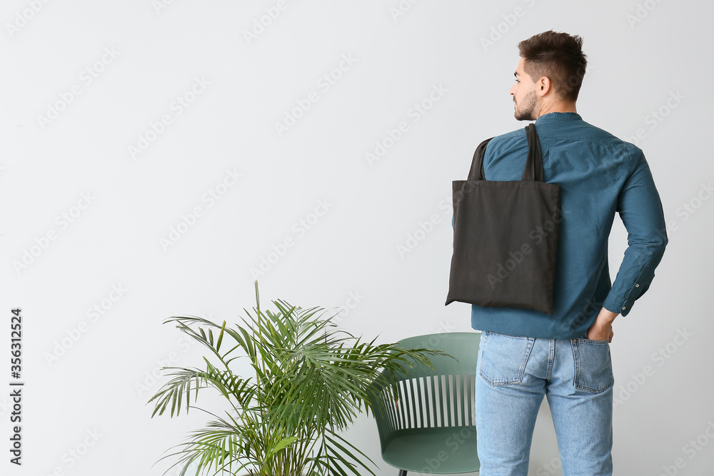 年轻人靠着浅色墙壁背着环保袋