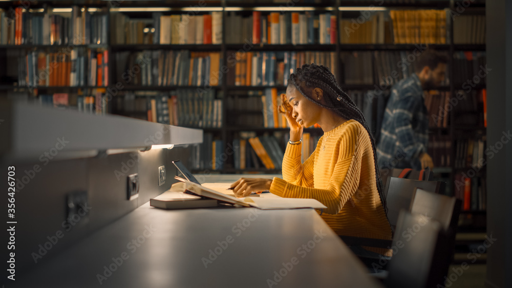 大学图书馆：天才黑人女孩使用笔记本电脑，为论文、论文、冲突研究写笔记
