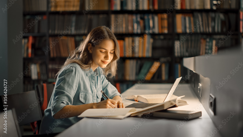 大学图书馆：漂亮聪明的高加索女孩使用笔记本电脑，为论文、论文和研究写笔记