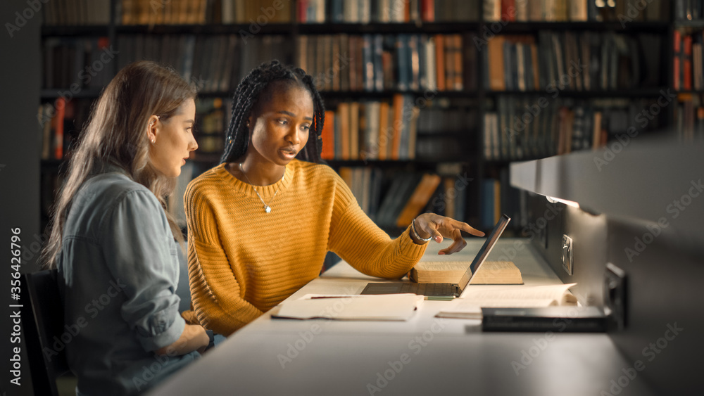 大学图书馆：两名天才女生学习，使用笔记本电脑，互相帮助提供建议