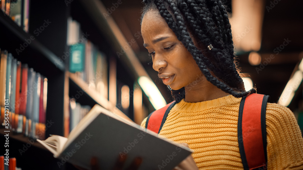 大学图书馆：聪明漂亮的黑人女孩站在书架旁拿着阅读文本B
