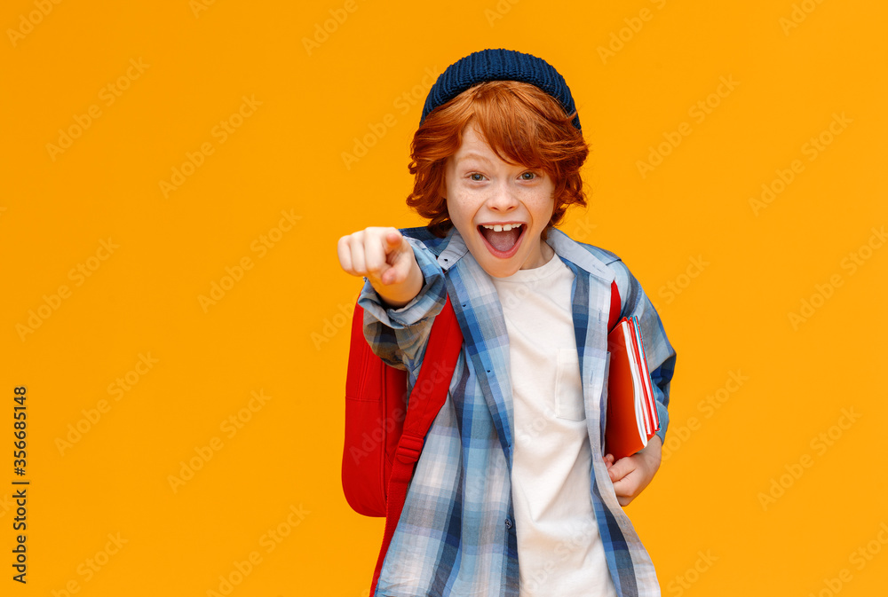 背着背包的姜黄色男孩惊讶地喊道，并指着黄色背景上隔离的摄像机