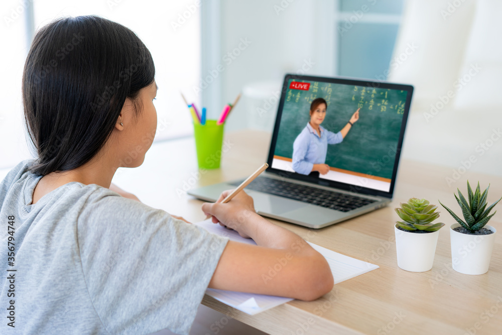 亚洲女学生与老师在家客厅的电脑上进行视频会议电子学习。主页