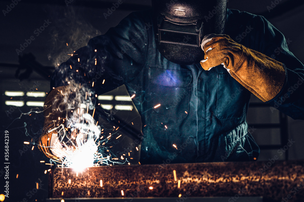 金属焊工在工厂使用电焊机焊接钢材，同时佩戴安全设备