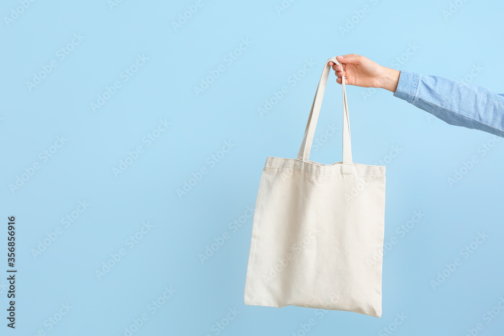 Female hand with eco bag on color background