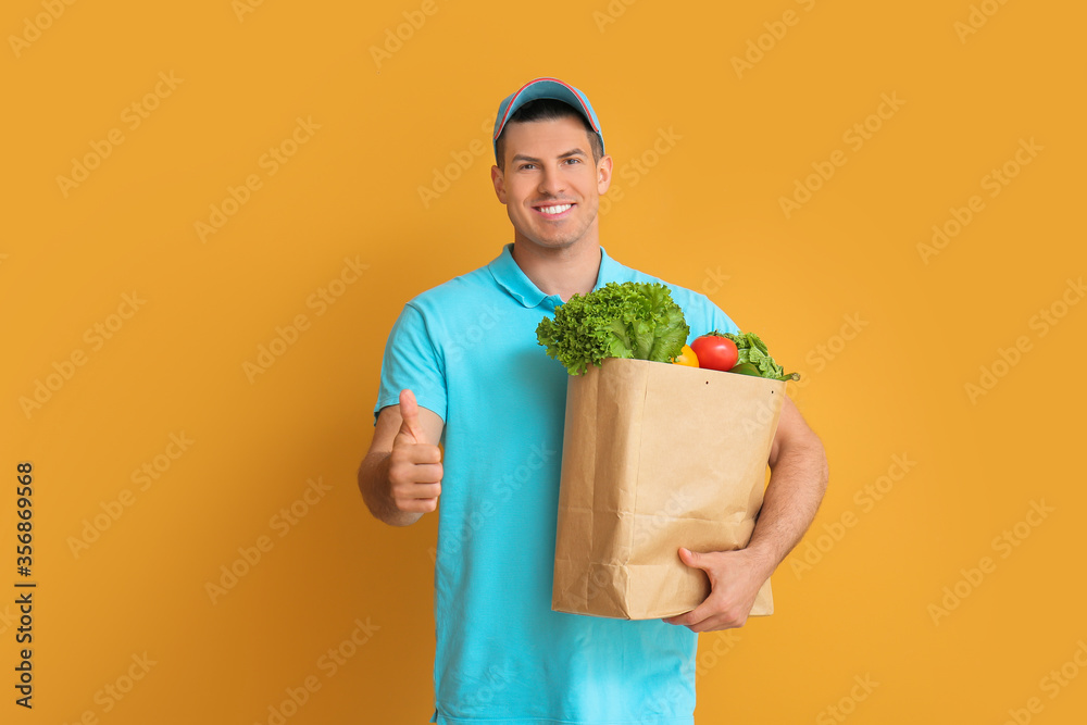 Delivery man with food in bag showing thumb-up gesture on color background