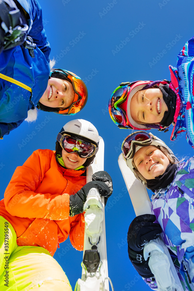 Group of children in ski in sport outfit mask ang helmets look down standing together over blue sky